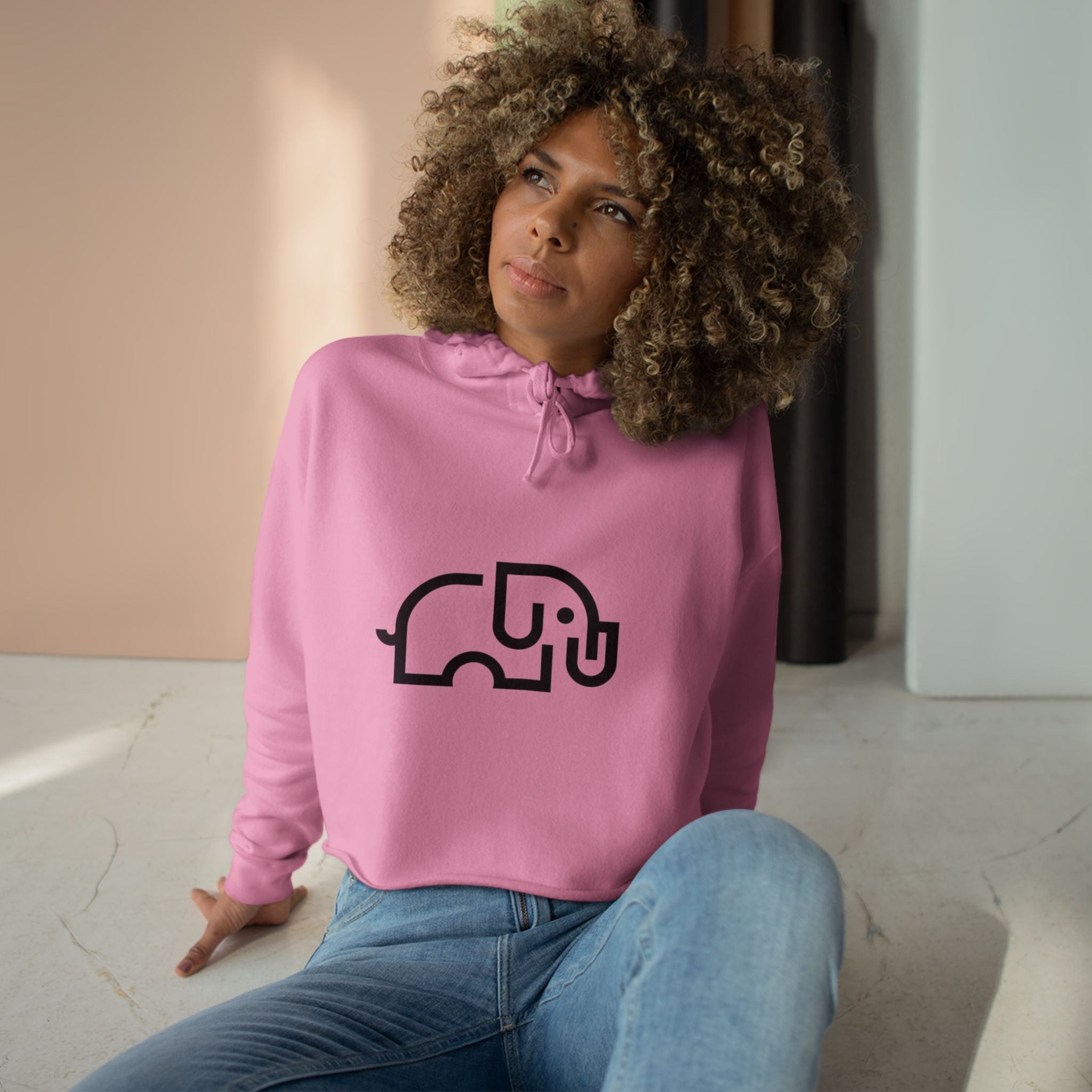 Women's pale pink cropped hoodie with minimalist single-line elephant graphic on chest, shown from front on female model