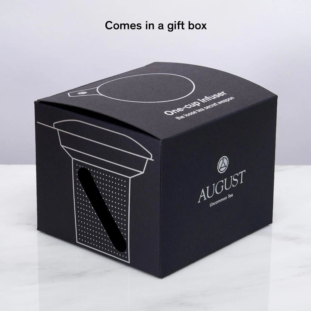 Stainless steel one-cup loose leaf tea infuser resting on its silicone lid coaster beside a ceramic mug