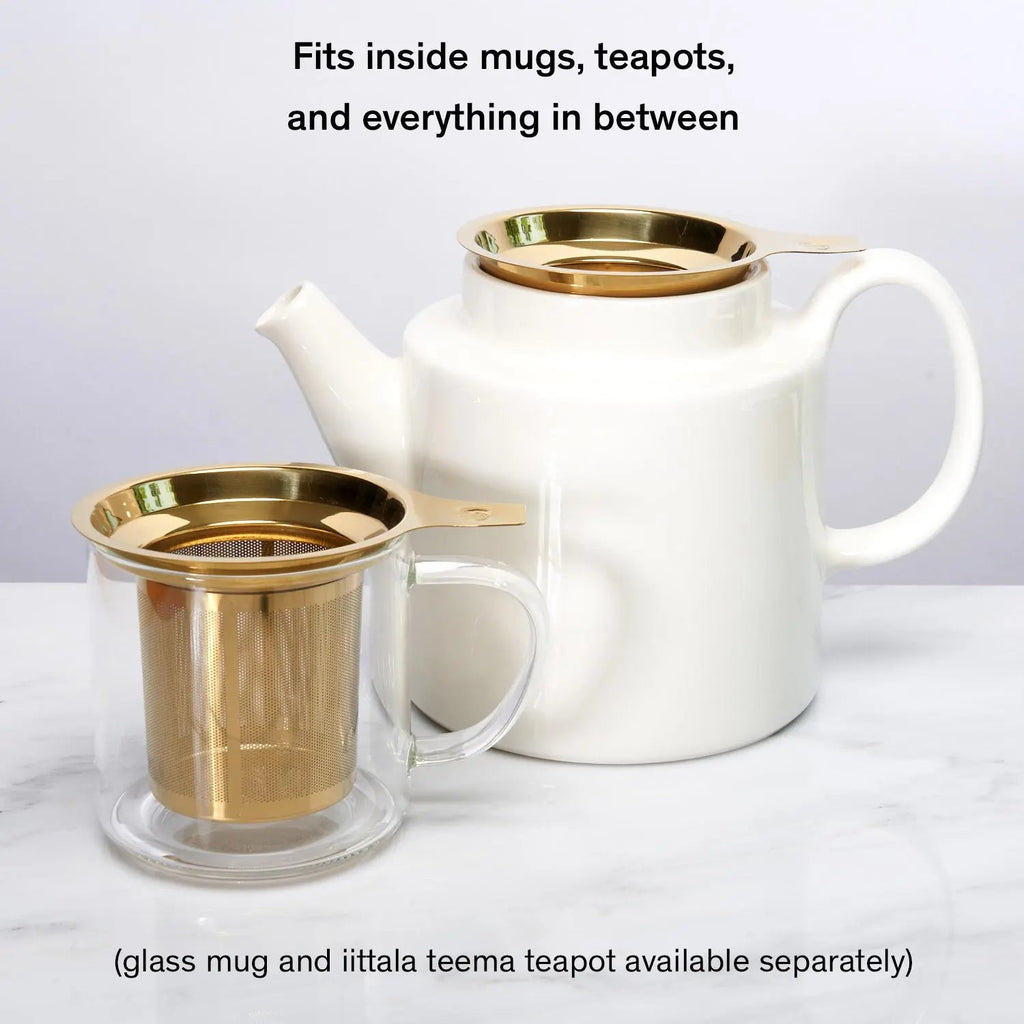 Stainless steel one-cup loose leaf tea infuser resting on its silicone lid coaster beside a ceramic mug