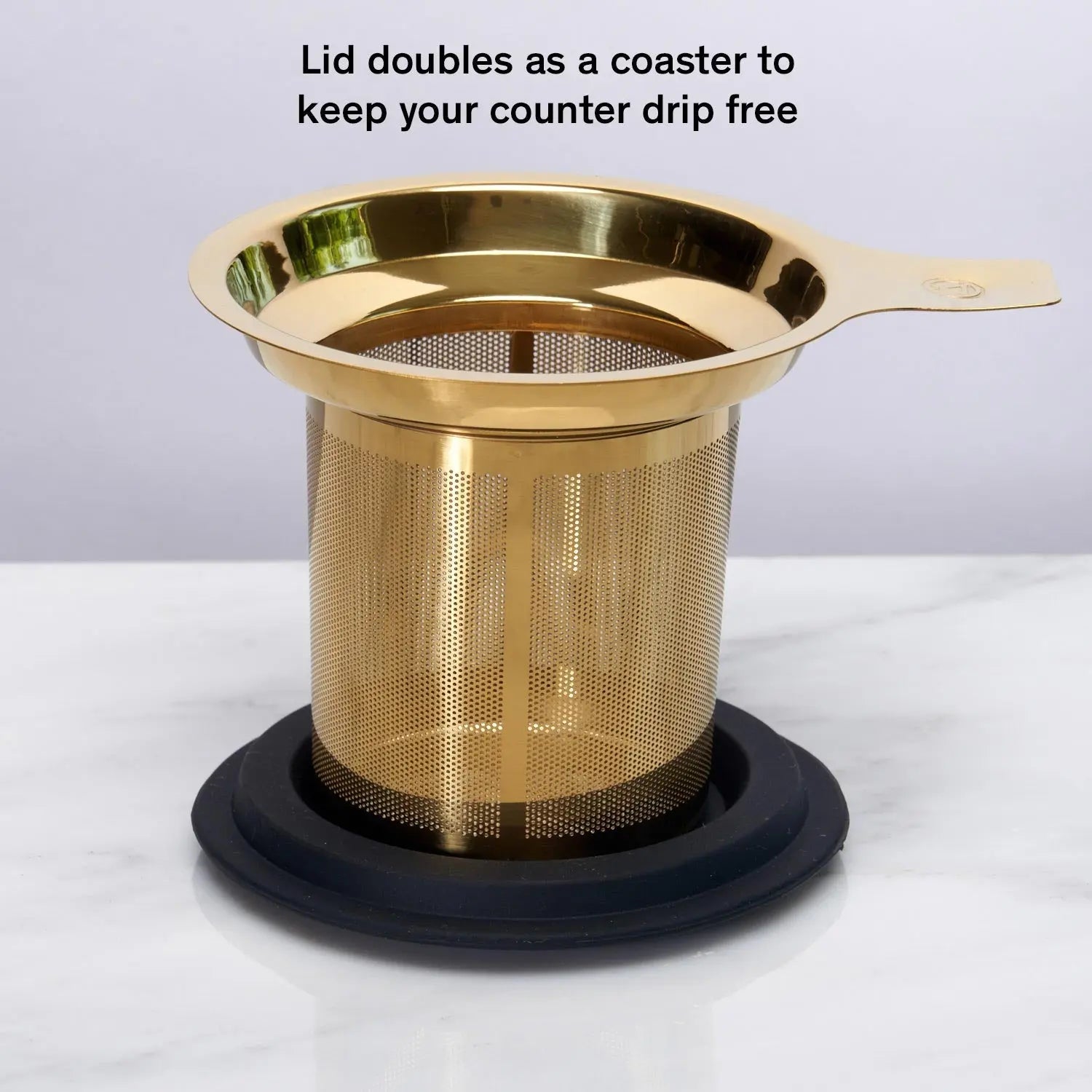 Stainless steel one-cup loose leaf tea infuser resting on its silicone lid coaster beside a ceramic mug