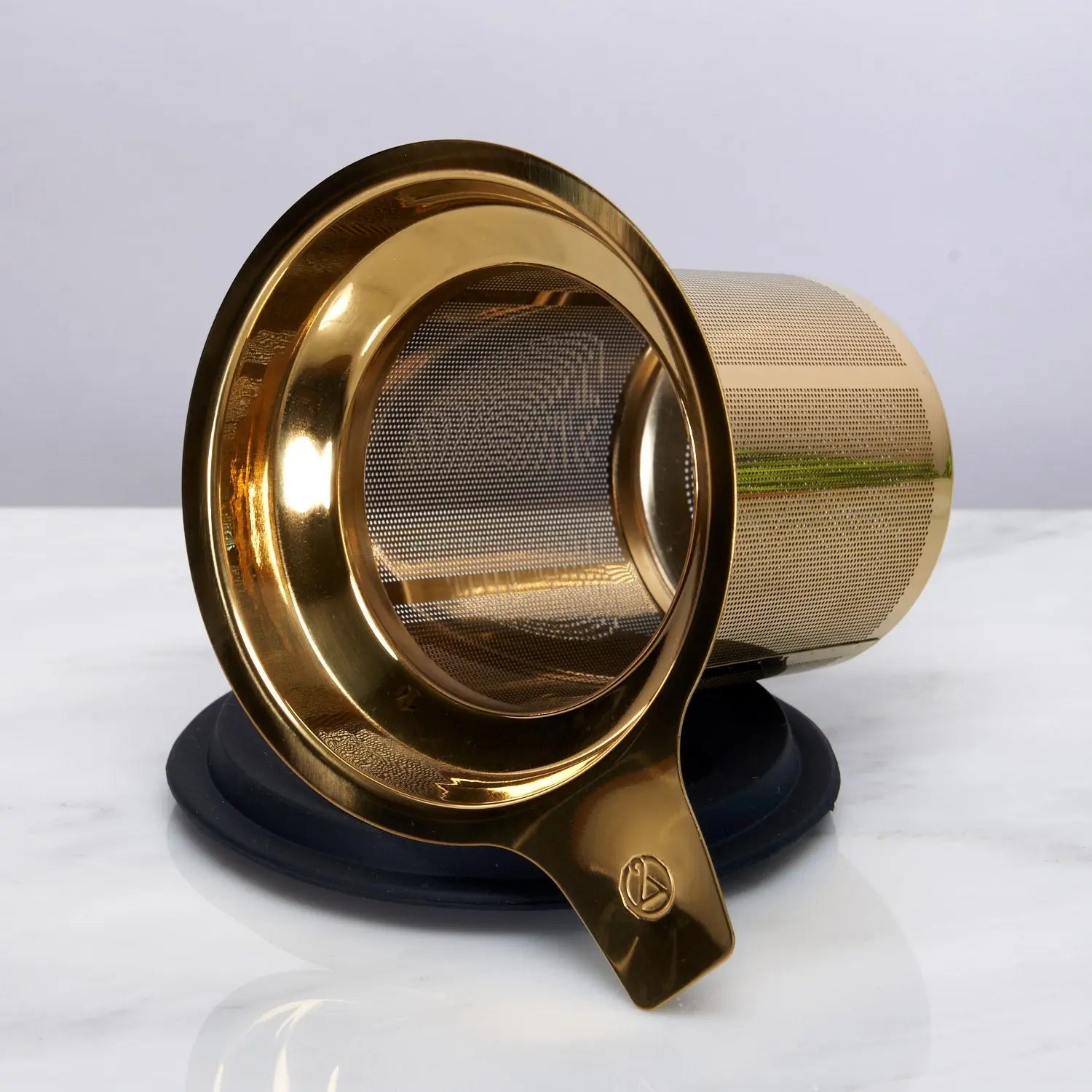 Stainless steel one-cup loose leaf tea infuser resting on its silicone lid coaster beside a ceramic mug