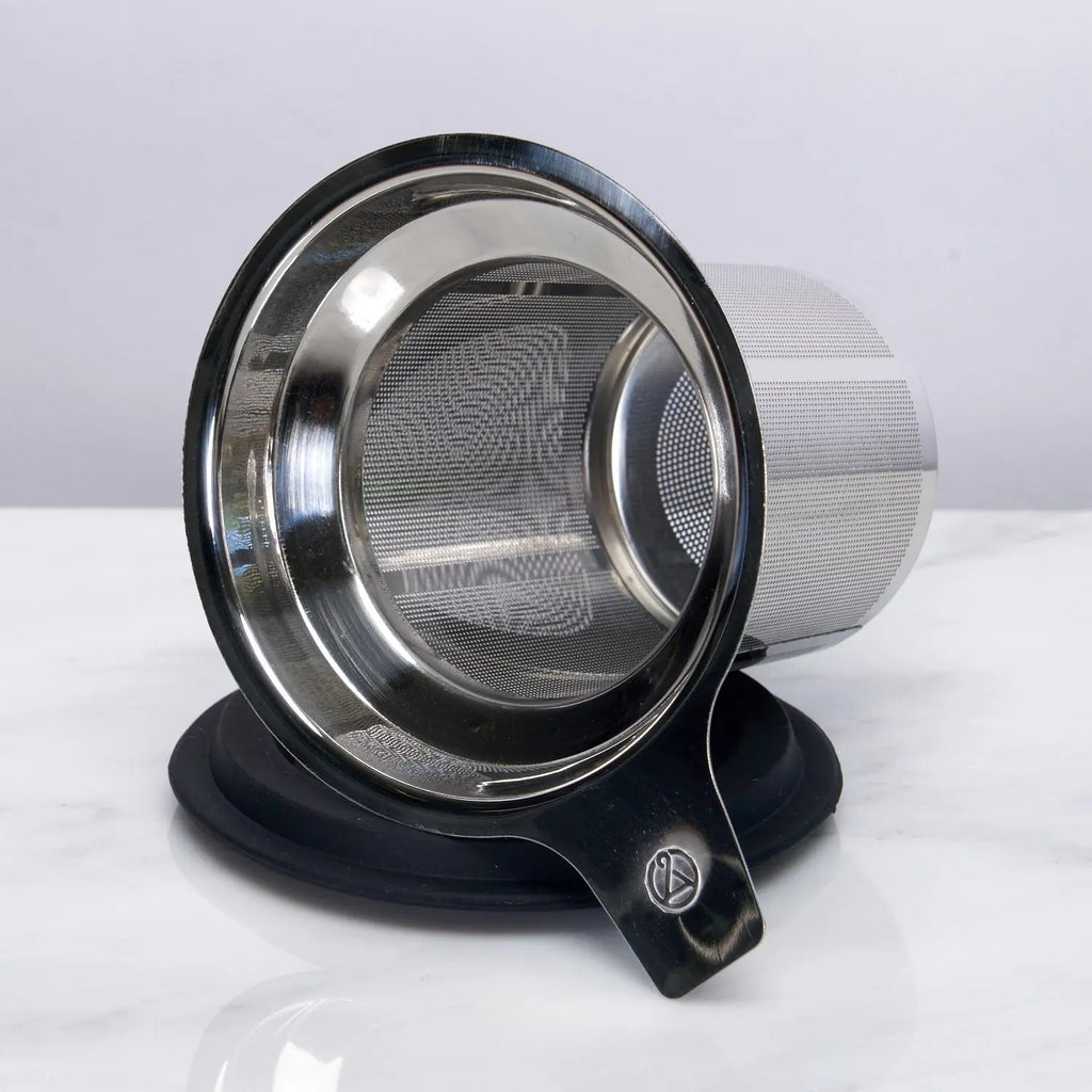 Stainless steel one-cup loose leaf tea infuser resting on its silicone lid coaster beside a ceramic mug