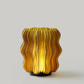 Cordless mini wavy sculptural table lamp with warm glowing filament on a nightstand