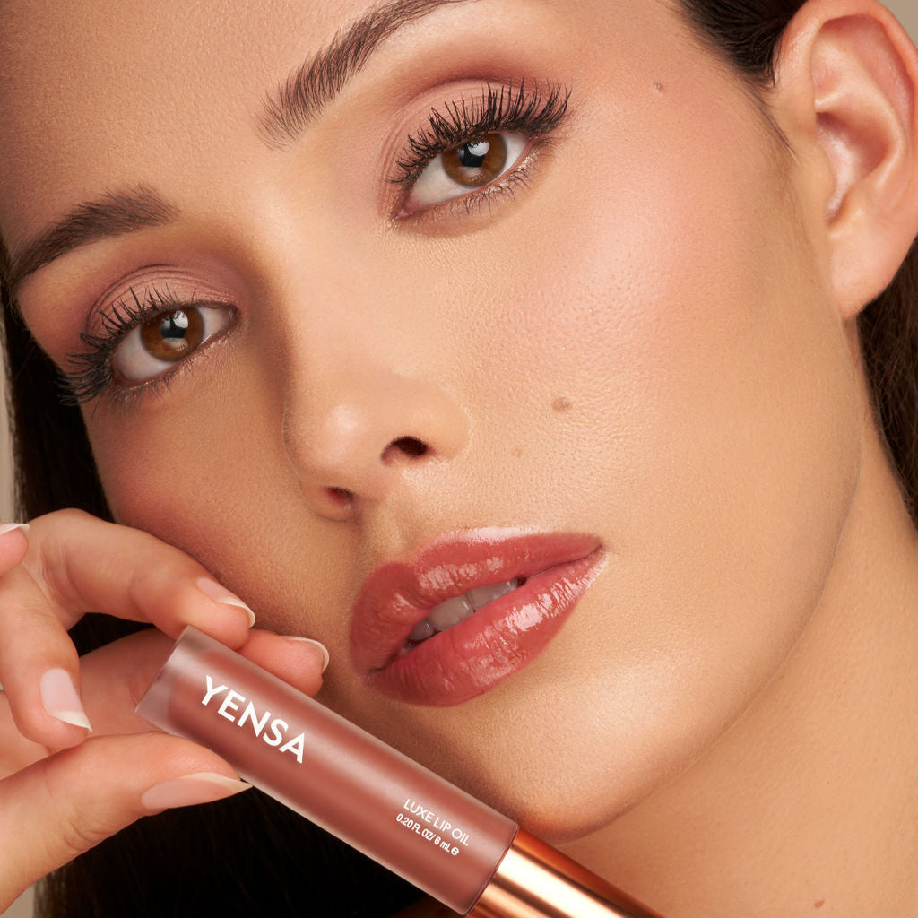 Close-up of tinted lip oil wand resting against soft-focus lips with a glossy, sheer finish
