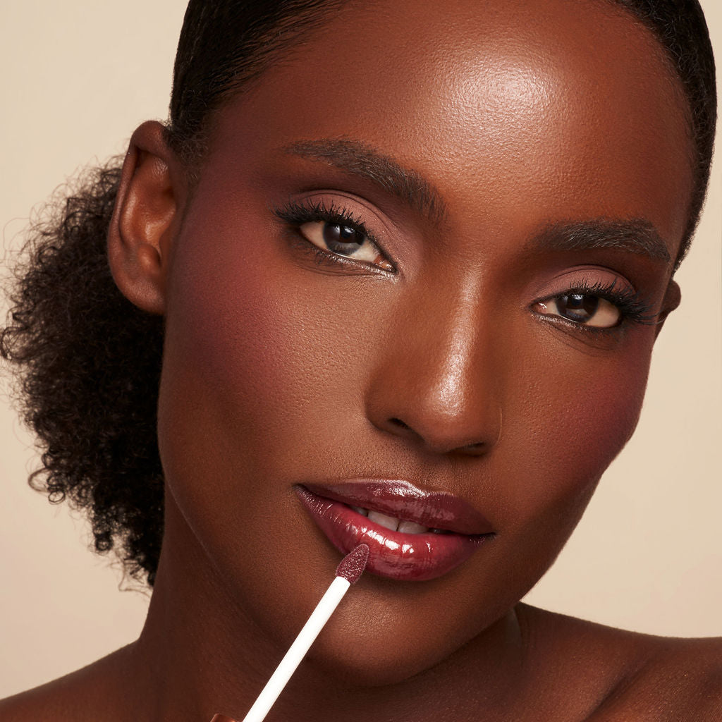 Close-up of tinted lip oil wand resting against soft-focus lips with a glossy, sheer finish