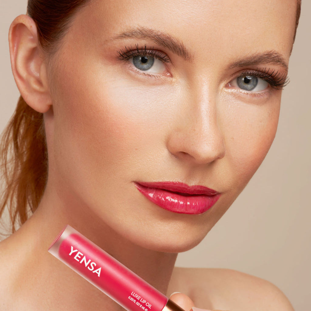 Close-up of tinted lip oil wand resting against soft-focus lips with a glossy, sheer finish