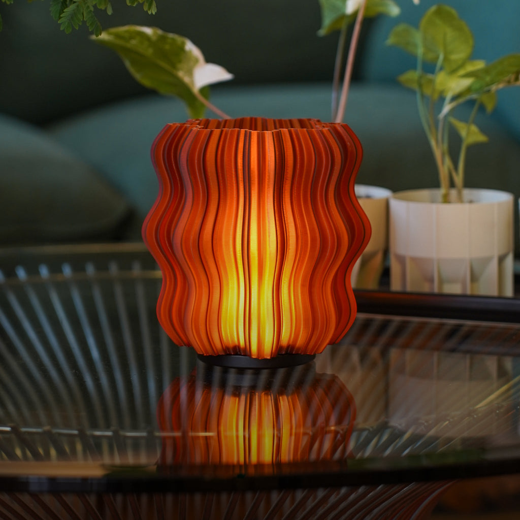 Cordless mini wavy sculptural table lamp with warm glowing filament on a nightstand