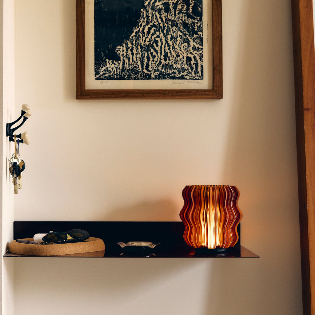 Cordless mini wavy sculptural table lamp with warm glowing filament on a nightstand