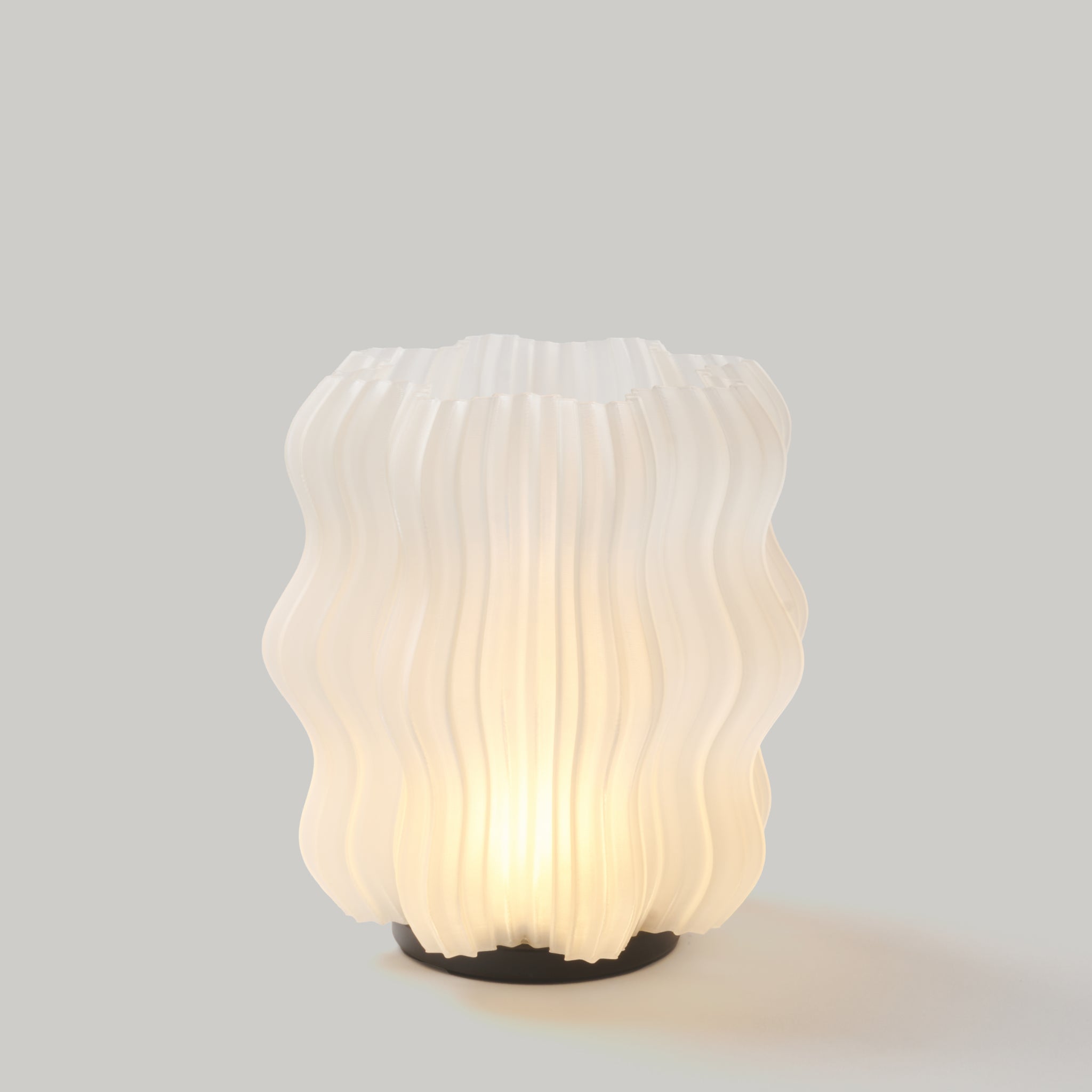 Cordless mini wavy sculptural table lamp with warm glowing filament on a nightstand