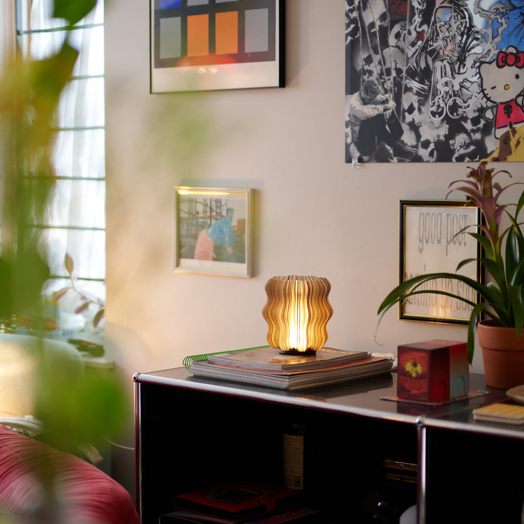 Cordless mini wavy sculptural table lamp with warm glowing filament on a nightstand