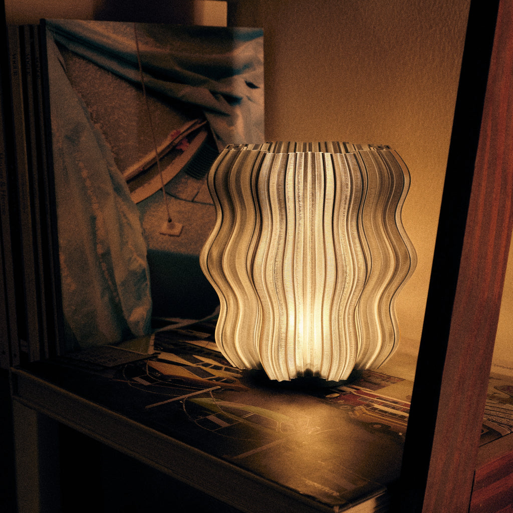 Cordless mini wavy sculptural table lamp with warm glowing filament on a nightstand