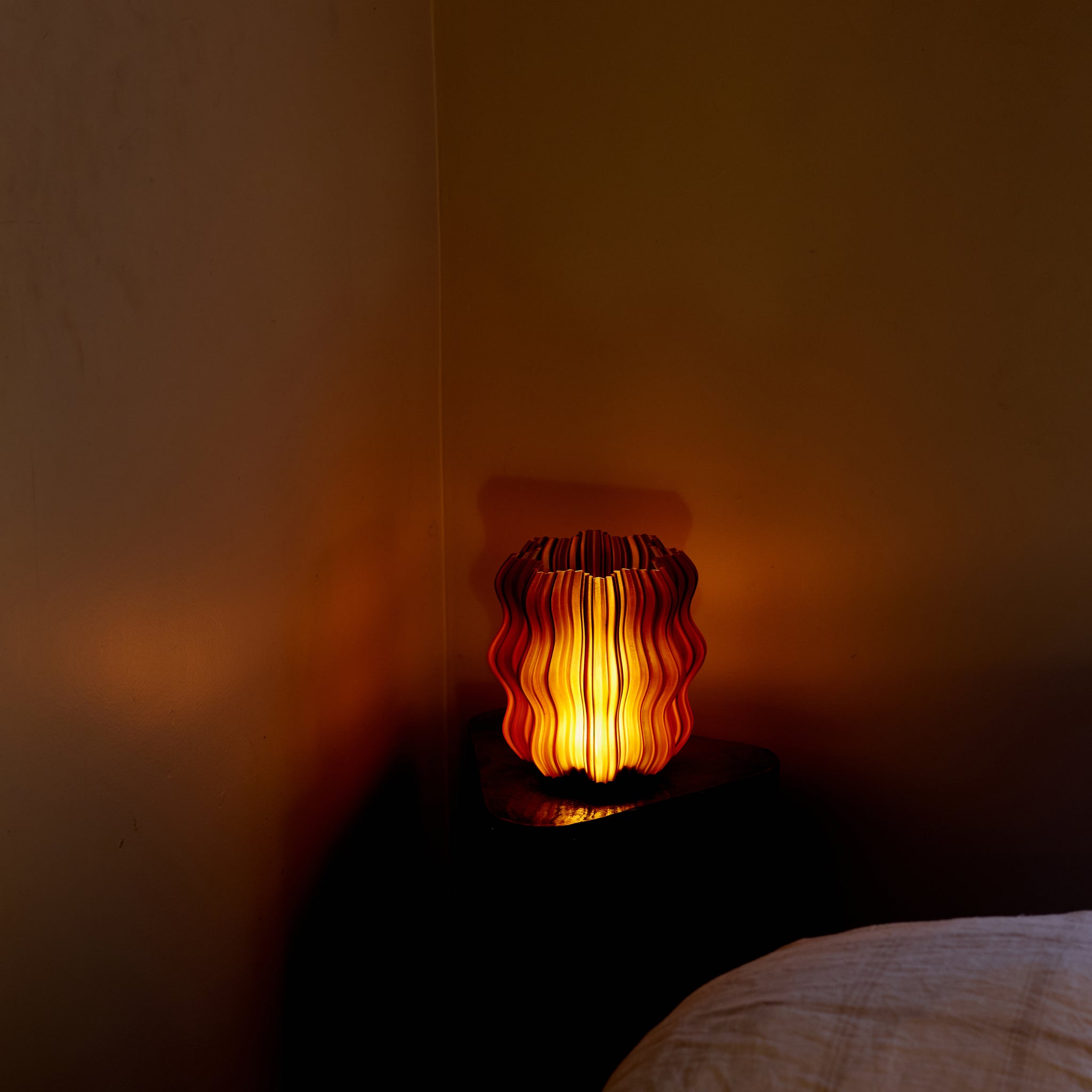 Cordless mini wavy sculptural table lamp with warm glowing filament on a nightstand
