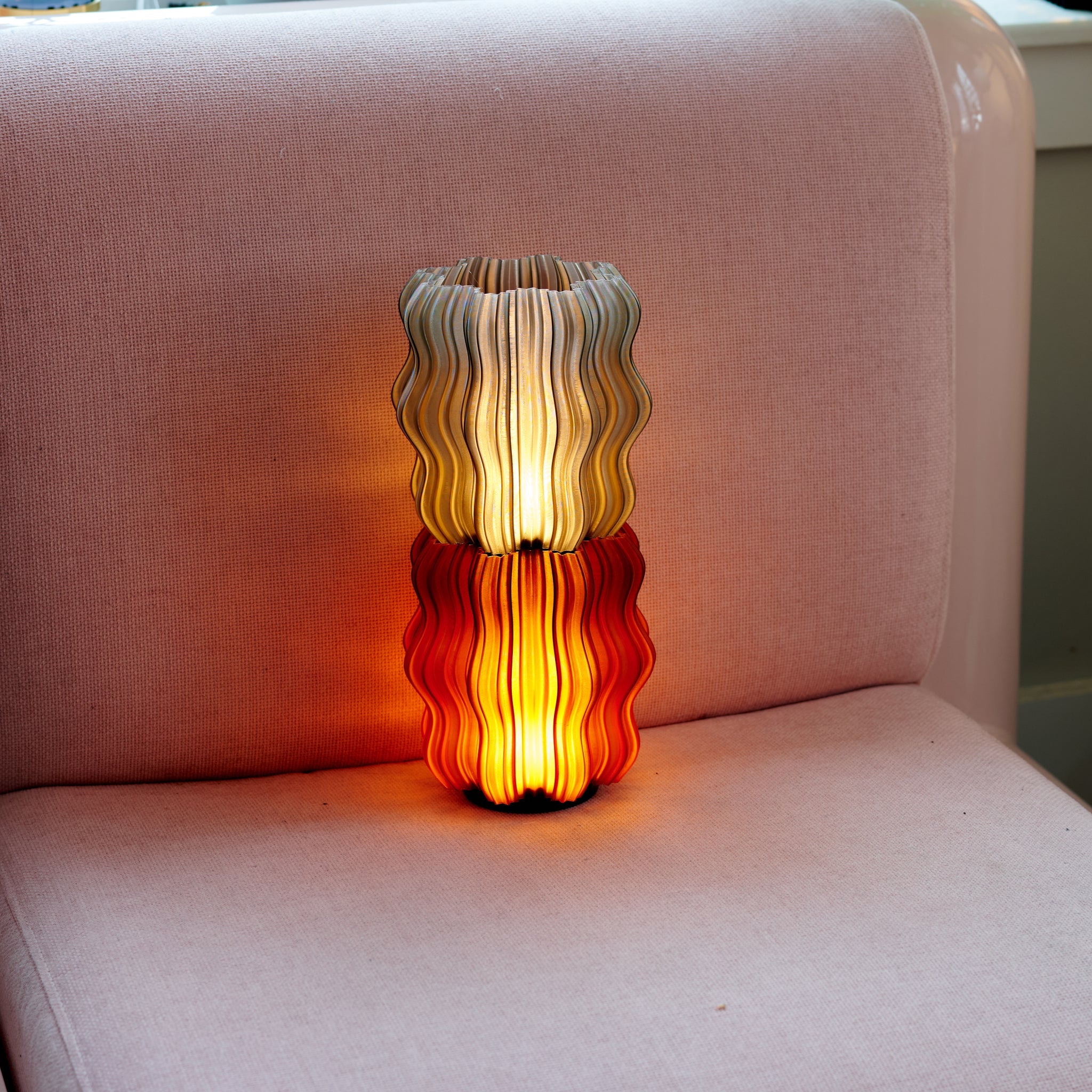 Cordless mini wavy sculptural table lamp with warm glowing filament on a nightstand