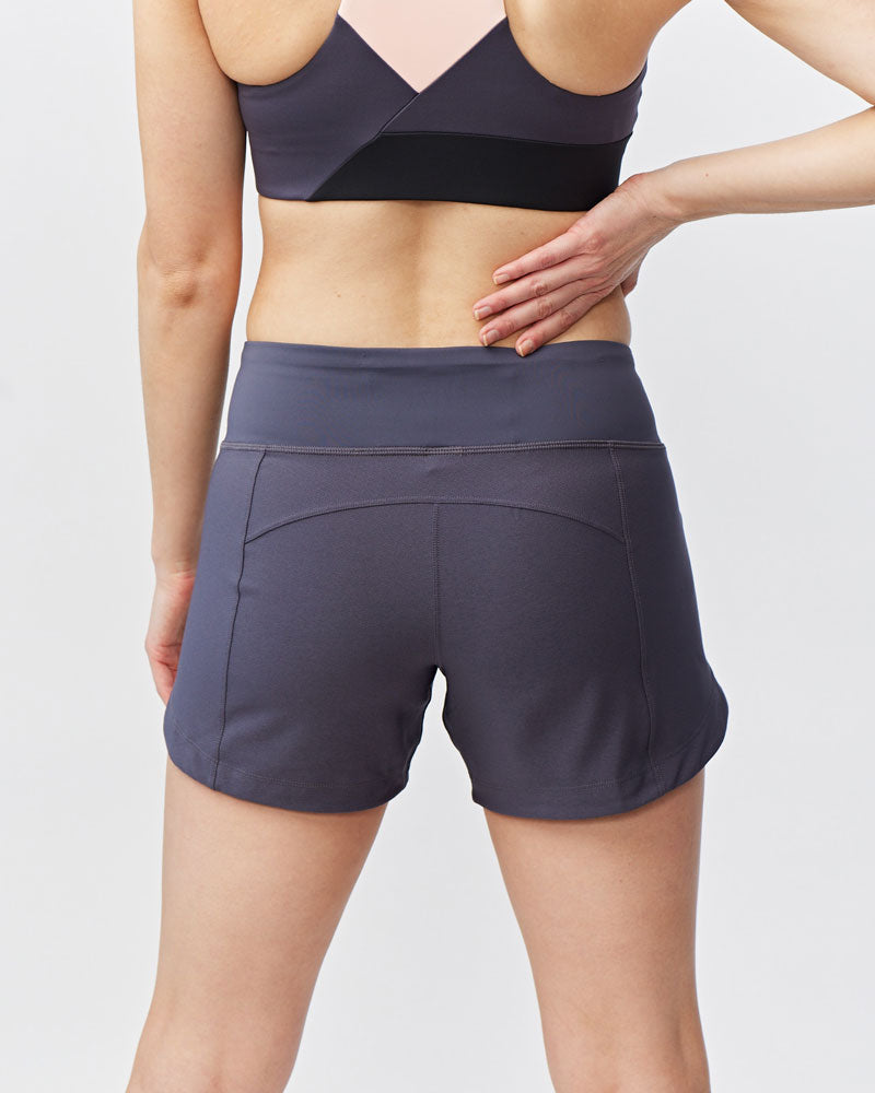 Women's Excel workout shorts in a relaxed training fit, showing extended hem length and waistband pocket detail