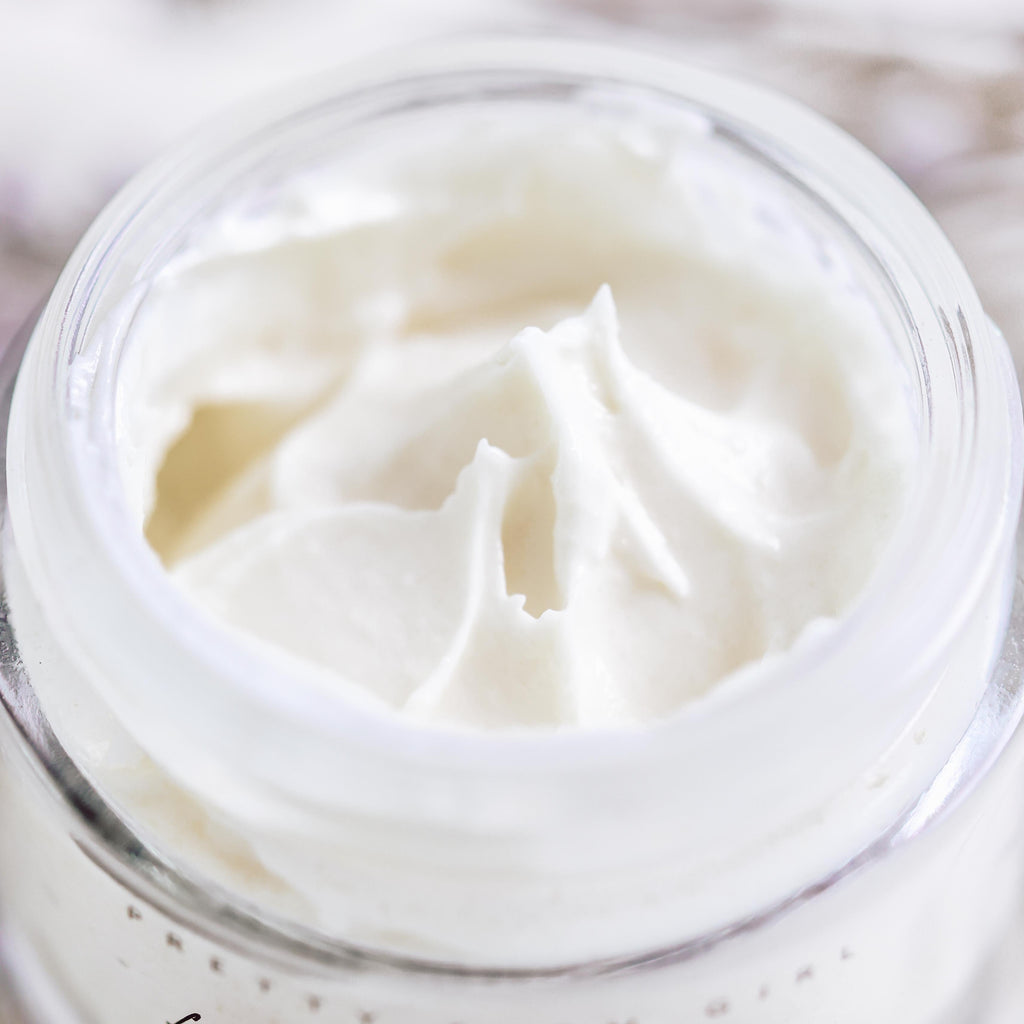 Small glass jar of tallow anti-aging face moisturizer with black lid on a clean surface