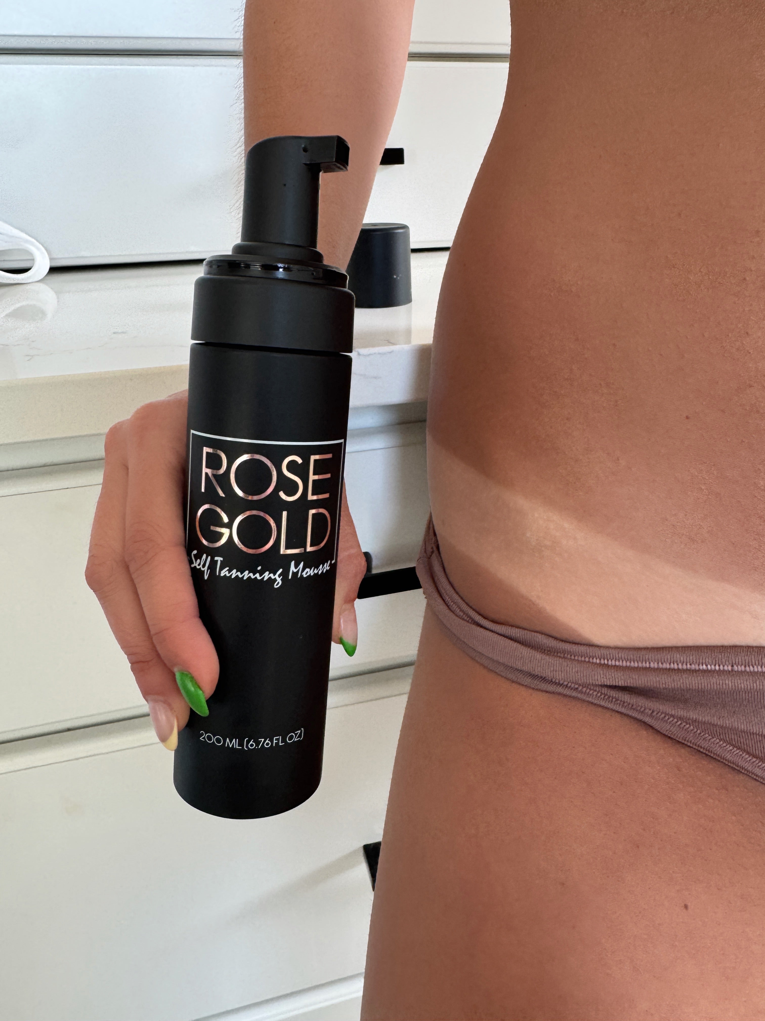 Dark neutral bronze self-tanning mousse in whipped foam texture, shown with applicator on light background