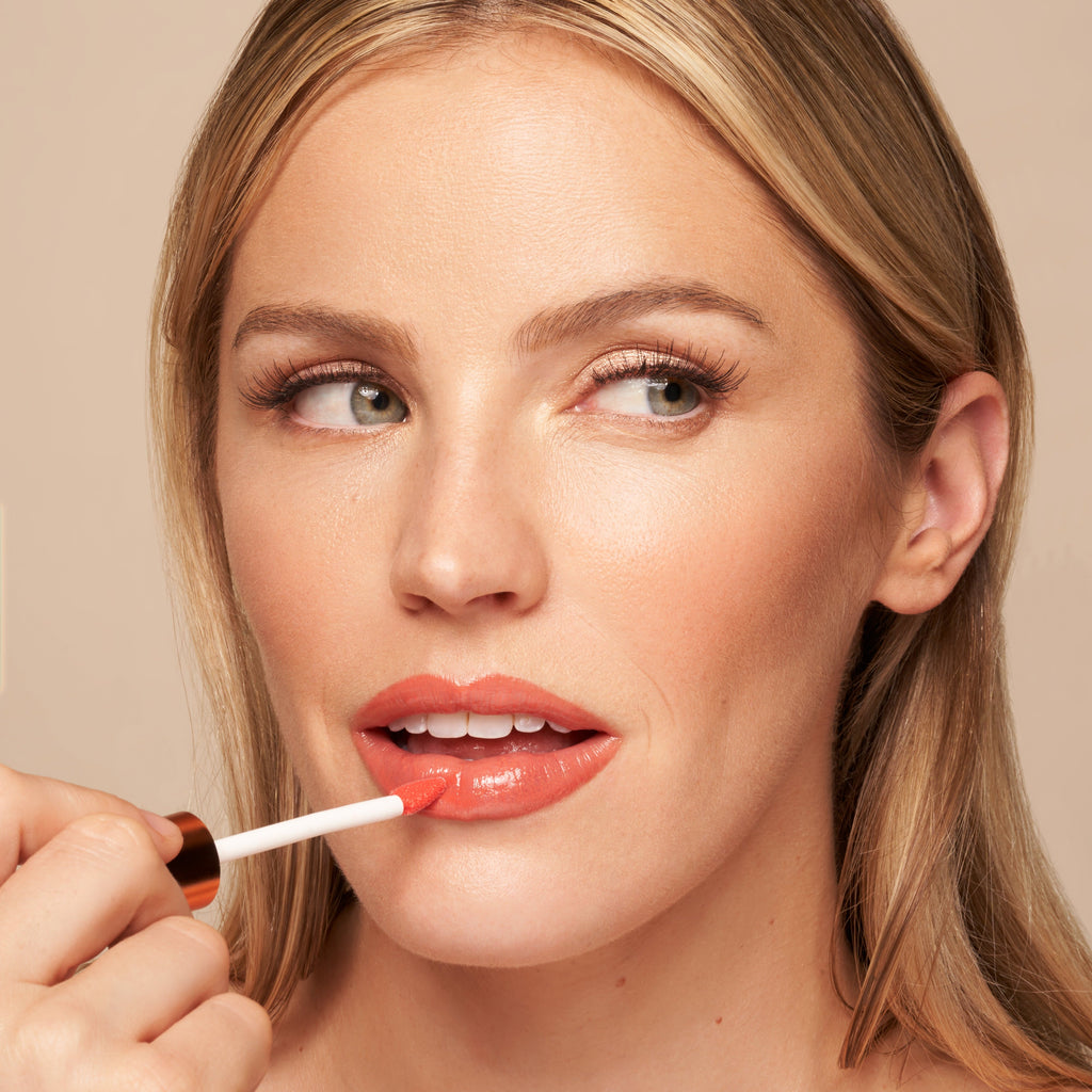 Close-up of tinted lip oil wand resting against soft-focus lips with a glossy, sheer finish