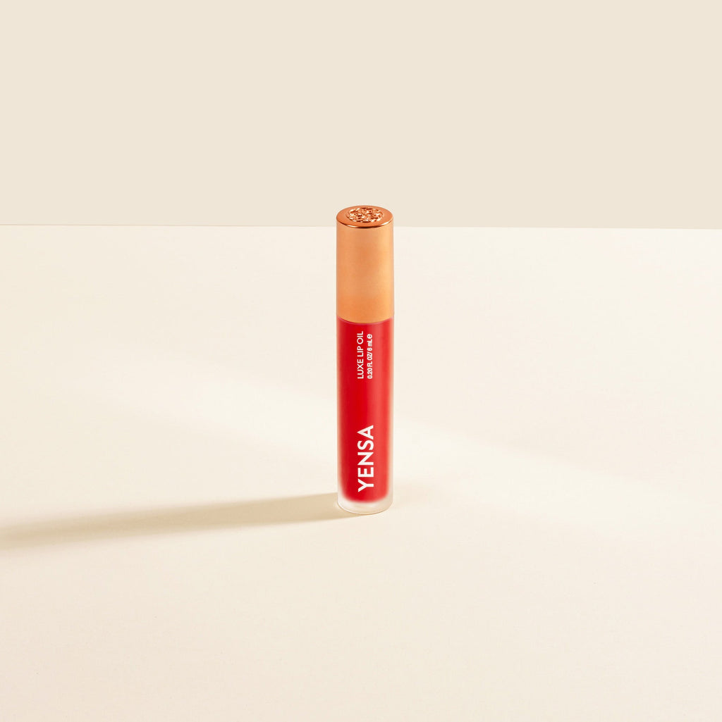 Close-up of tinted lip oil wand resting against soft-focus lips with a glossy, sheer finish