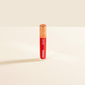 Close-up of tinted lip oil wand resting against soft-focus lips with a glossy, sheer finish