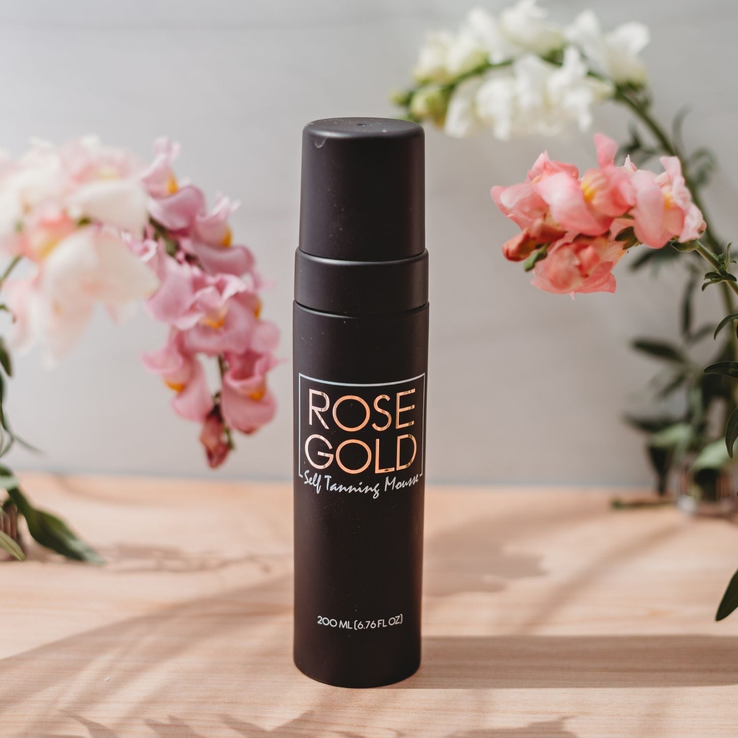 Dark neutral bronze self-tanning mousse in whipped foam texture, shown with applicator on light background