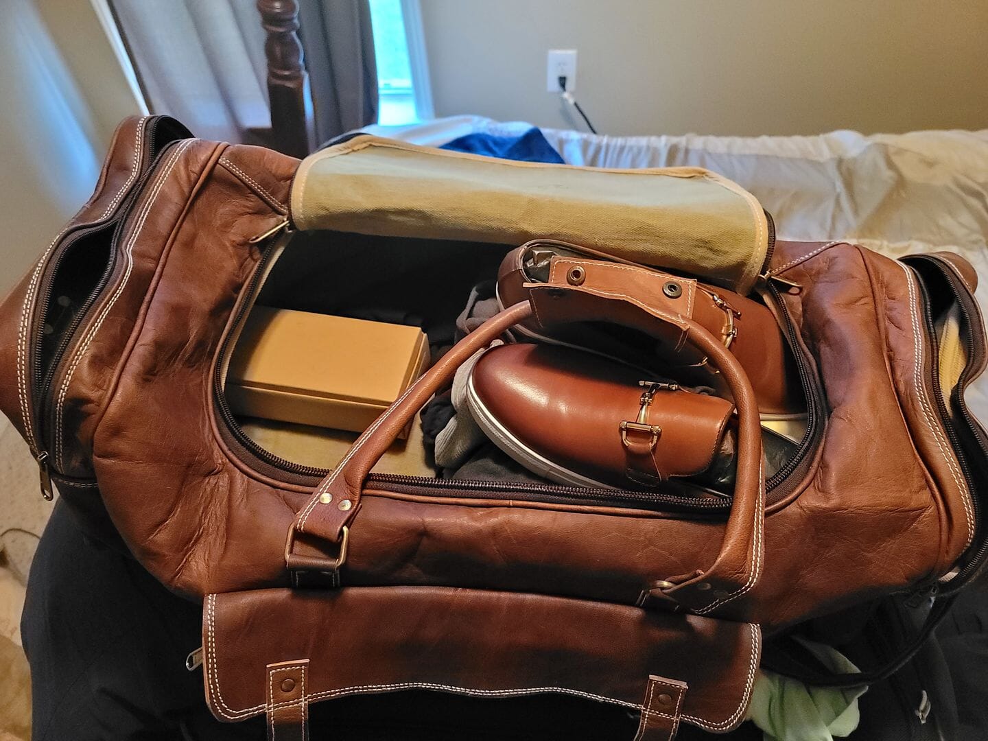 Vintage brown full-grain goat leather weekender duffle bag with brass hardware and matching toiletry bag on neutral background