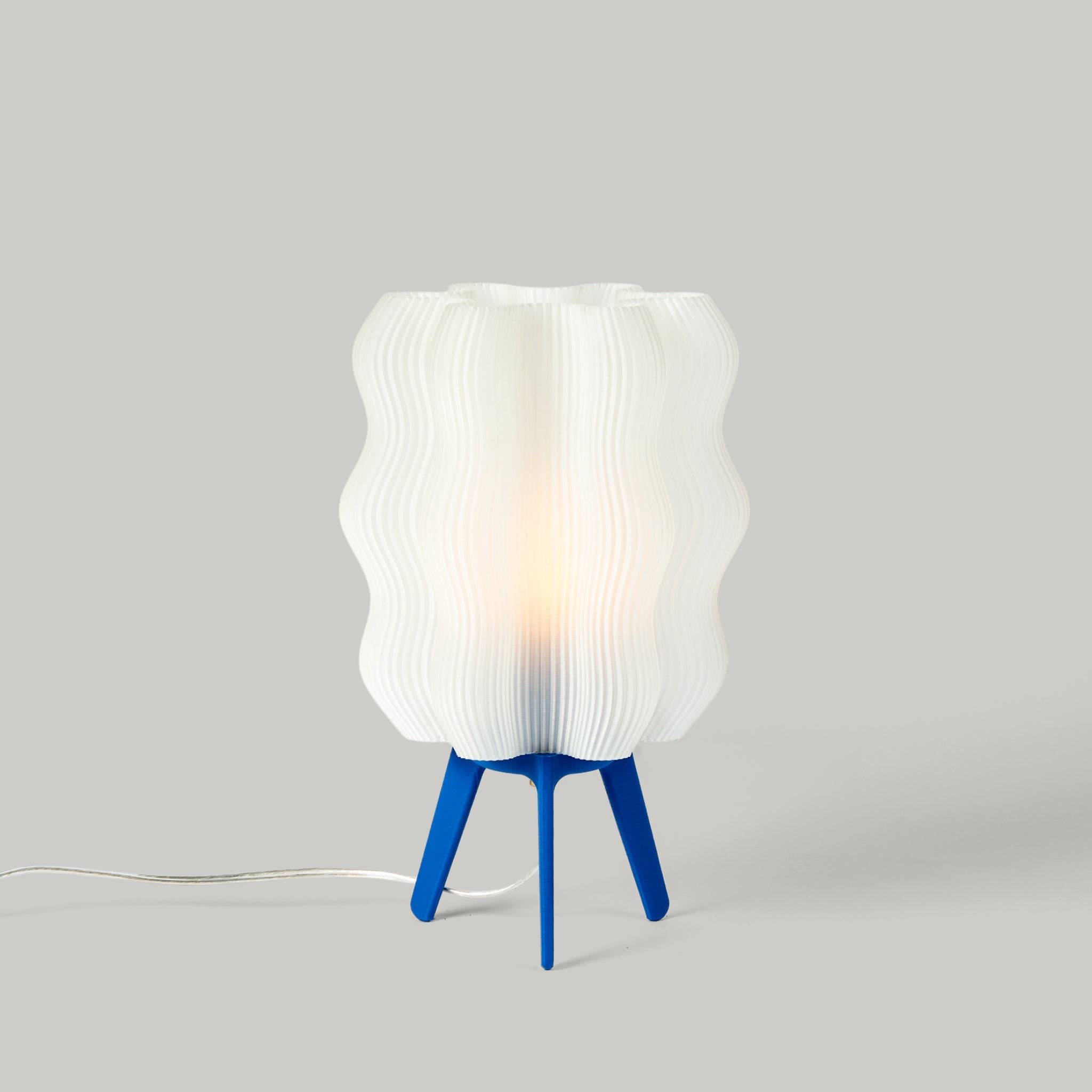 Wavy sculptural table lamp in recycled corn-based plastic with organic rippled silhouette on a flat surface