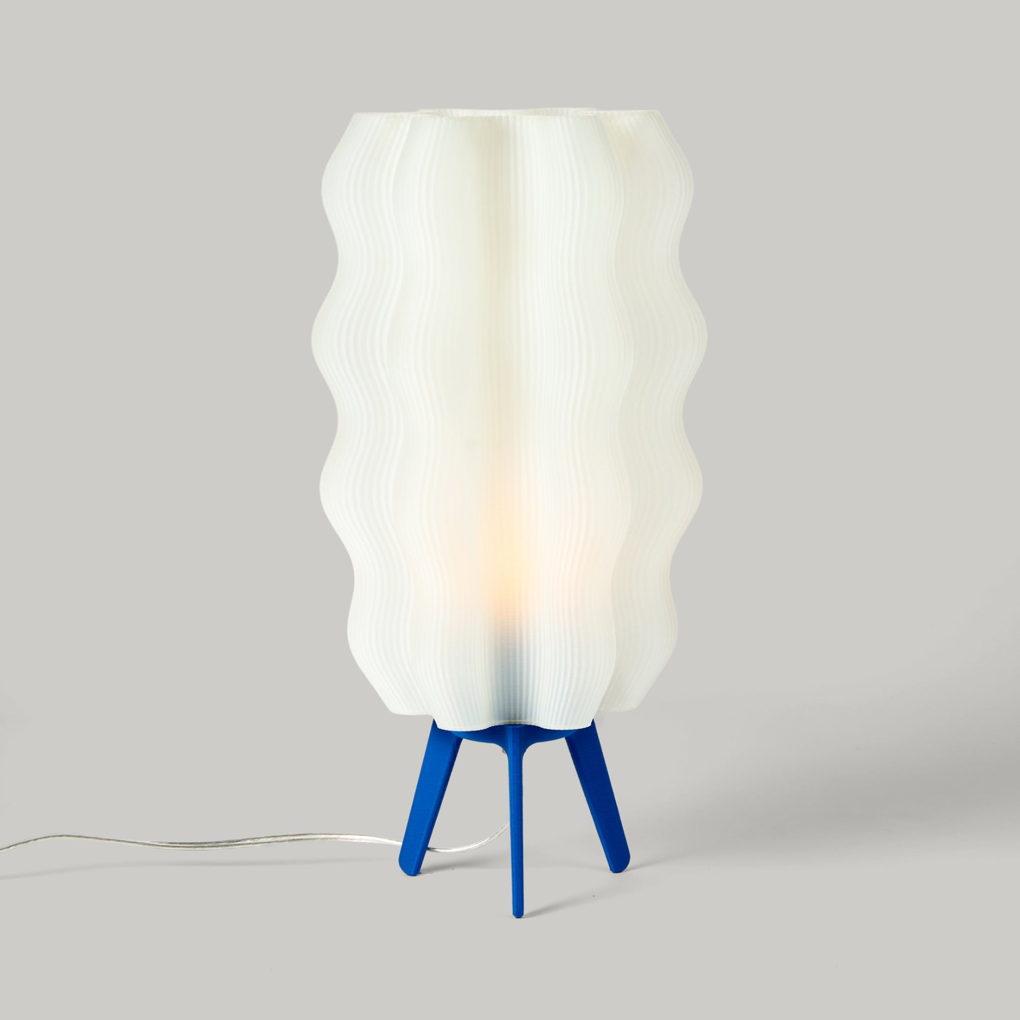 Wavy sculptural table lamp in recycled corn-based plastic with organic rippled silhouette on a flat surface