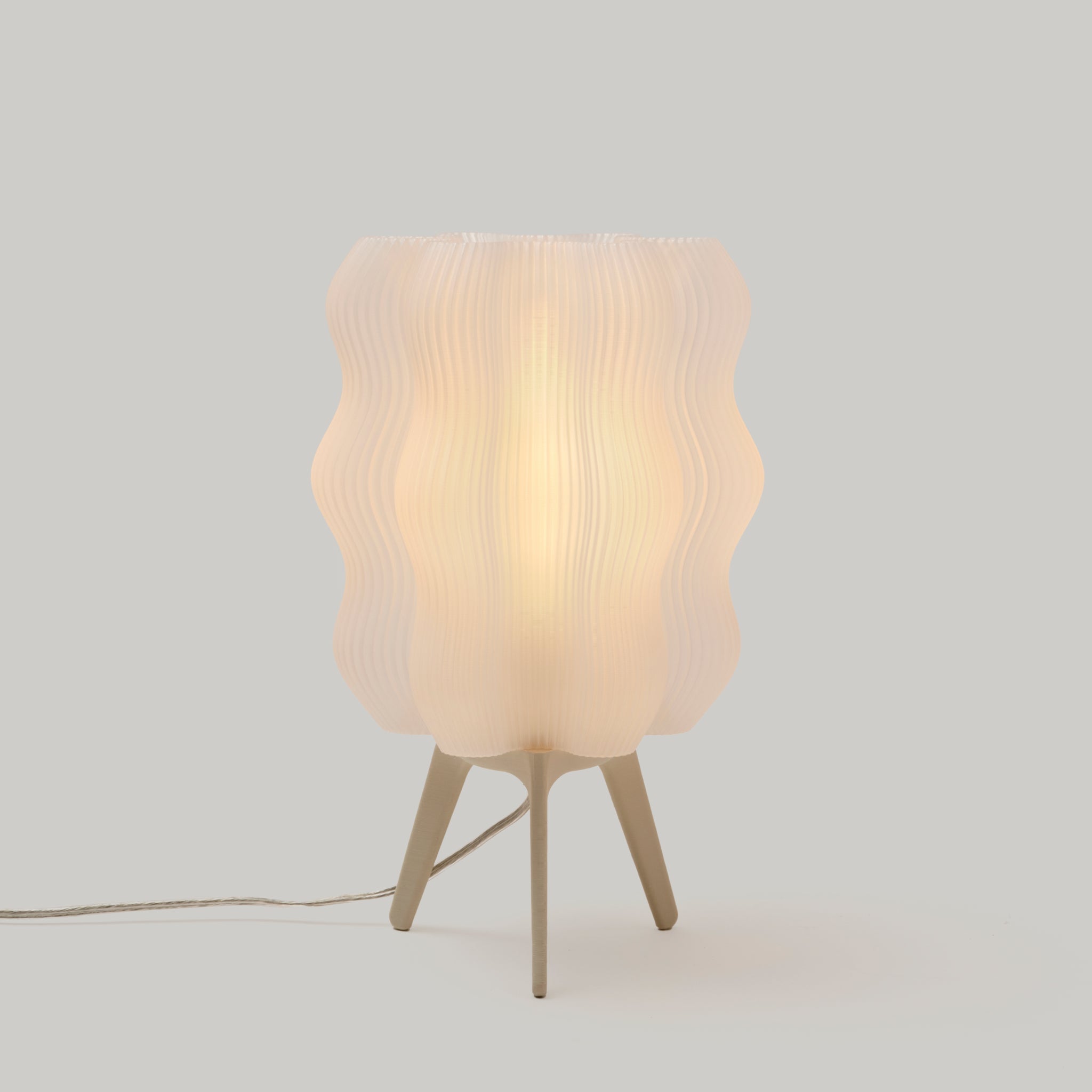 Wavy sculptural table lamp in recycled corn-based plastic with organic rippled silhouette on a flat surface