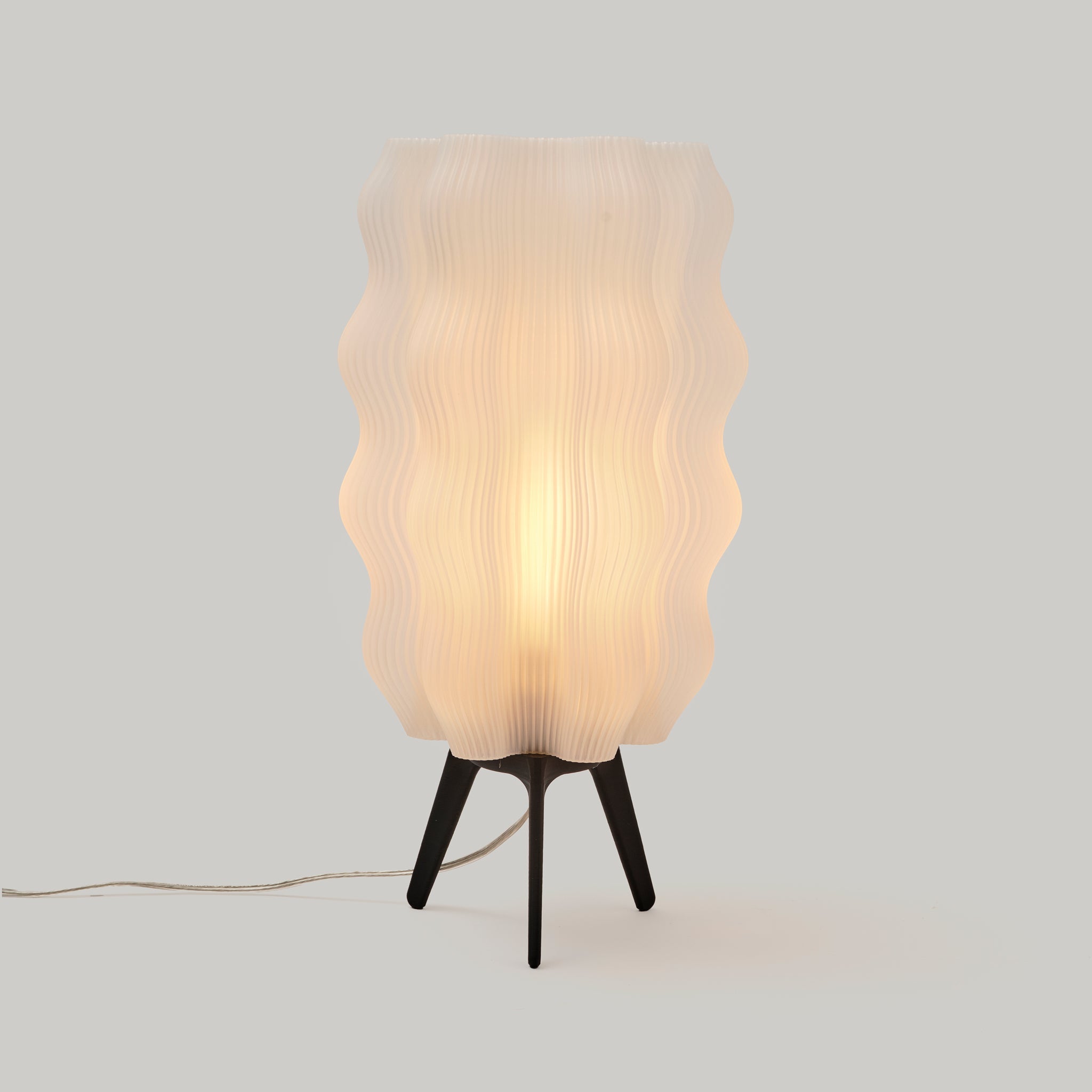 Wavy sculptural table lamp in recycled corn-based plastic with organic rippled silhouette on a flat surface