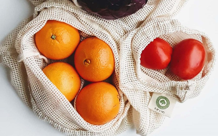 Set of reusable organic cotton mesh produce bags in multiple sizes filled with fresh vegetables