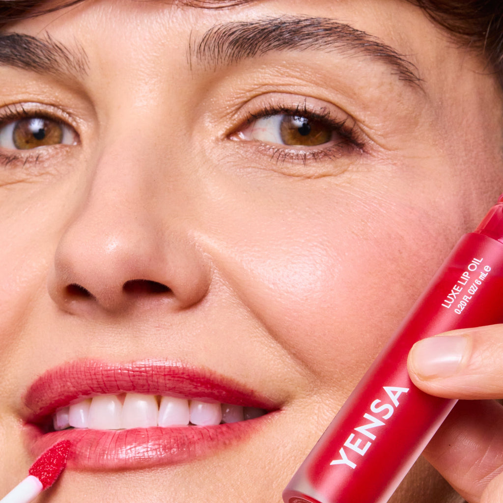 Close-up of tinted lip oil wand resting against soft-focus lips with a glossy, sheer finish