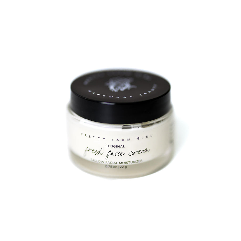 Small glass jar of tallow anti-aging face moisturizer with black lid on a clean surface