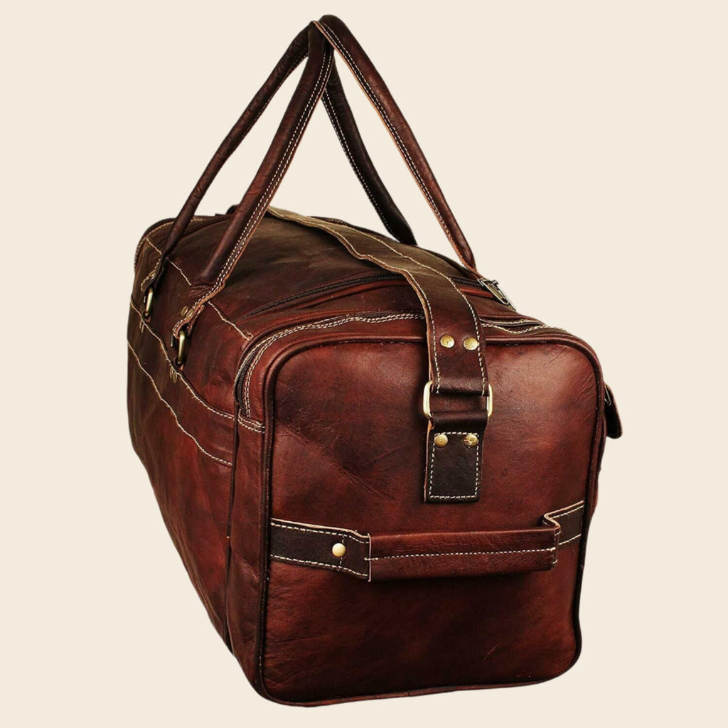 Vintage brown full-grain goat leather weekender duffle bag with brass hardware and matching toiletry bag on neutral background