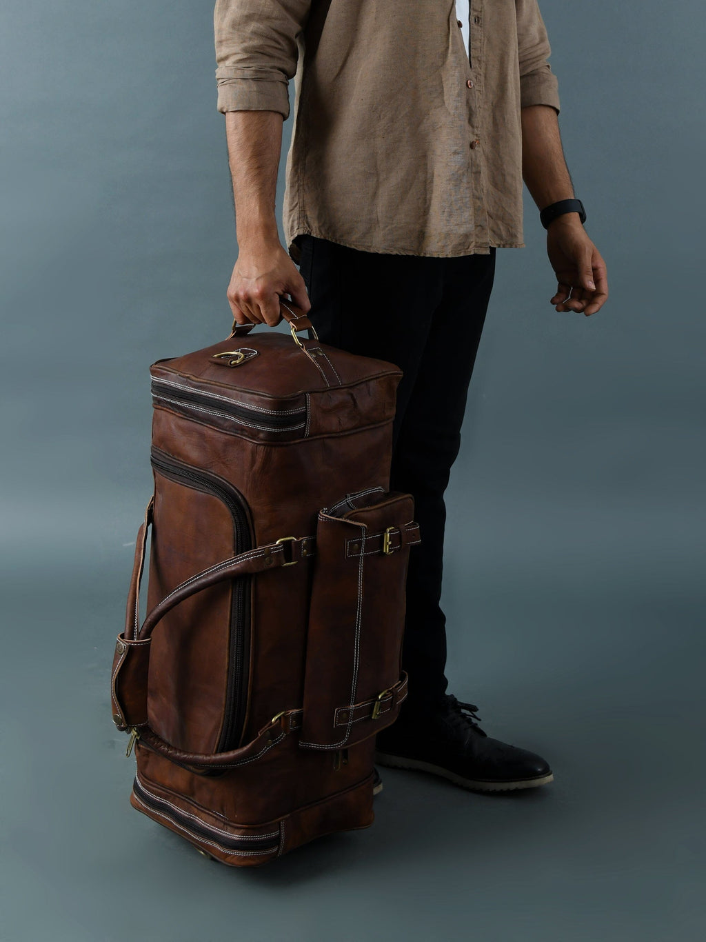 Vintage brown full-grain goat leather weekender duffle bag with brass hardware and matching toiletry bag on neutral background