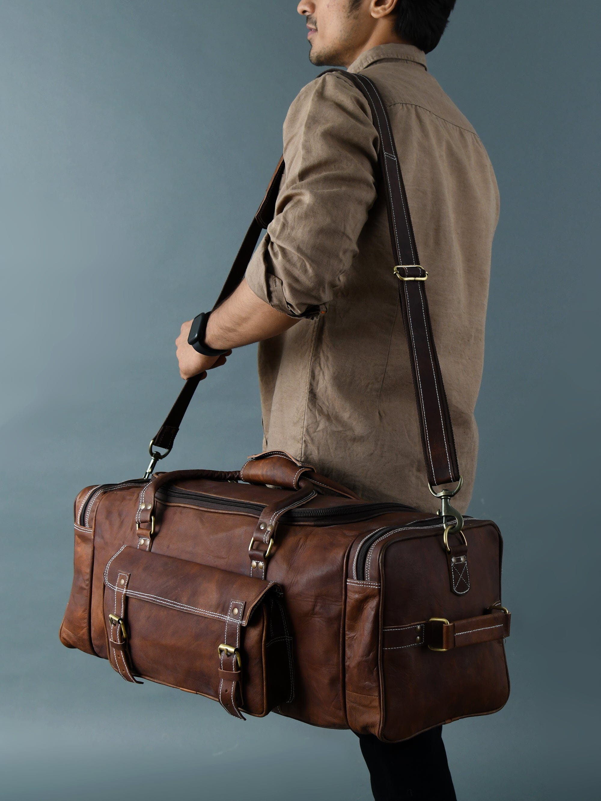 Vintage brown full-grain goat leather weekender duffle bag with brass hardware and matching toiletry bag on neutral background