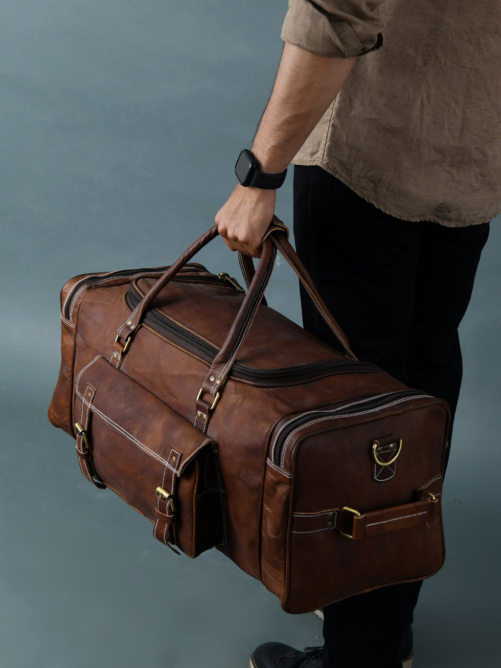 Vintage brown full-grain goat leather weekender duffle bag with brass hardware and matching toiletry bag on neutral background