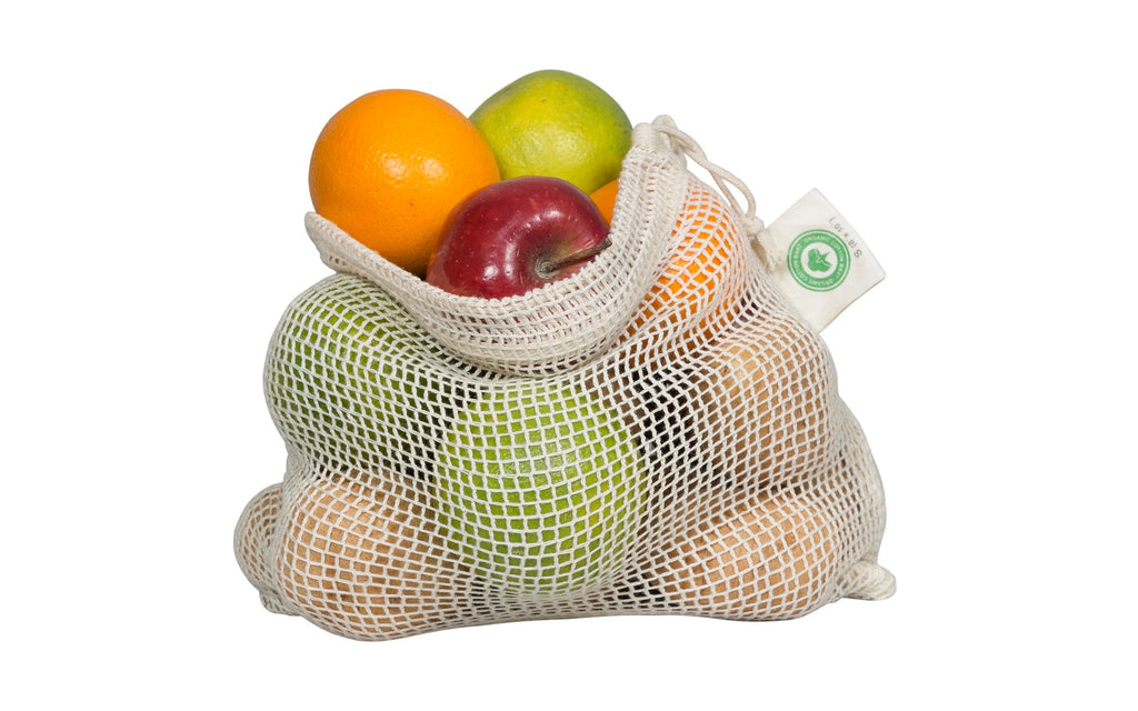 Set of reusable organic cotton mesh produce bags in multiple sizes filled with fresh vegetables
