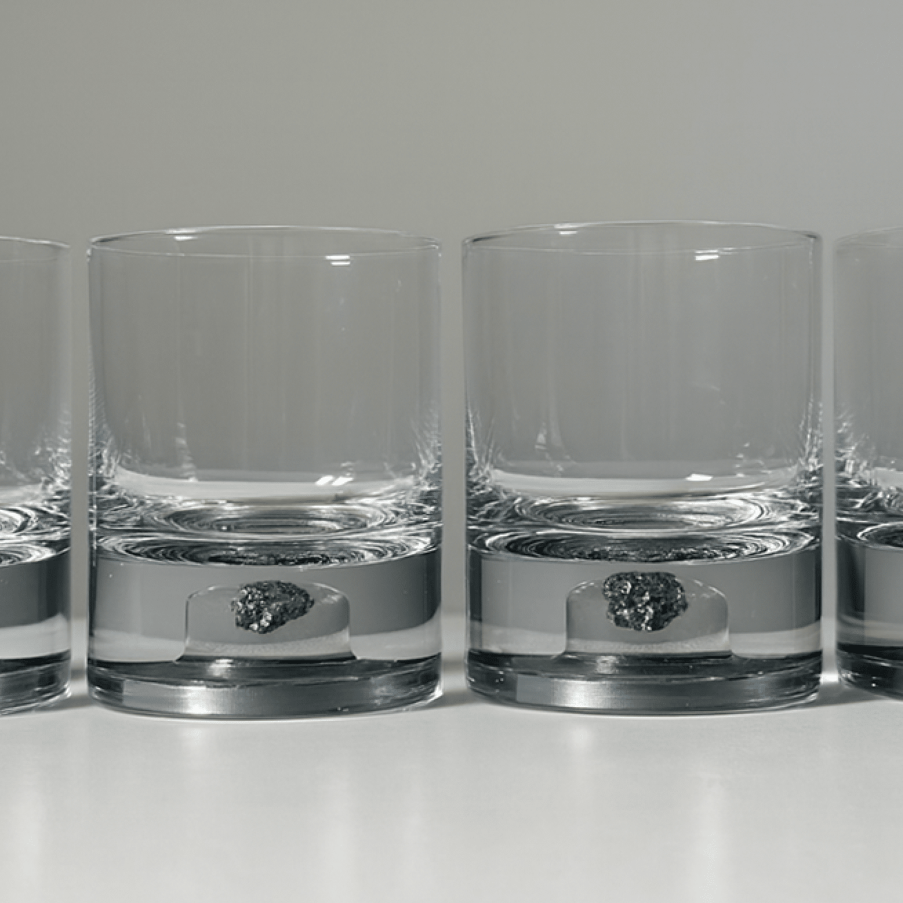 Set of two glass tumblers with genuine meteorite fragments suspended in high-clarity bases, shown in Antique Tin and Amber Gold finishes