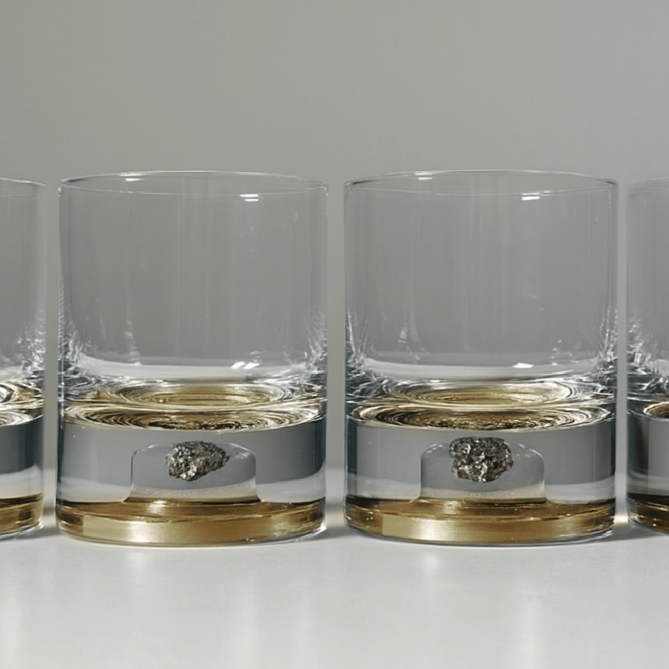 Set of two glass tumblers with genuine meteorite fragments suspended in high-clarity bases, shown in Antique Tin and Amber Gold finishes
