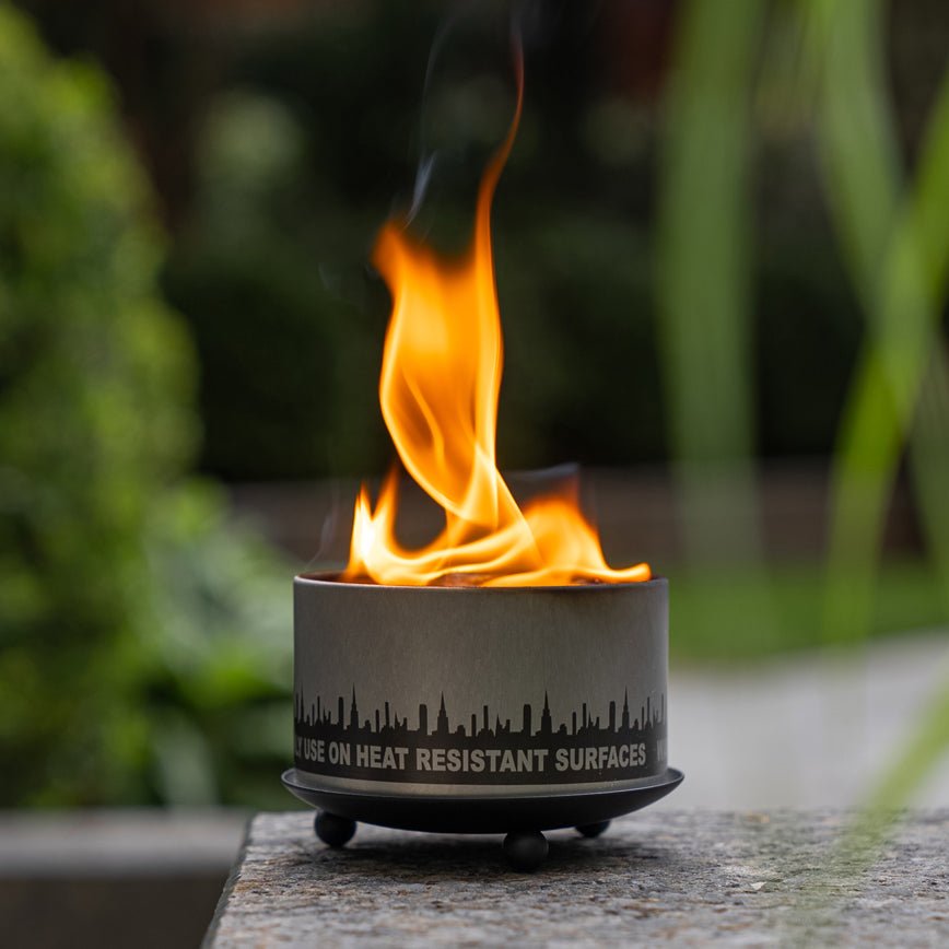 Matte black wrought iron trivet and candle holder with three ball feet on a neutral surface