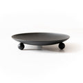 Matte black wrought iron trivet and candle holder with three ball feet on a neutral surface