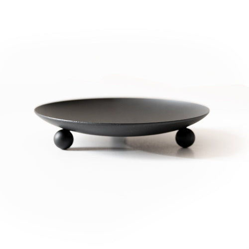 Matte black wrought iron trivet and candle holder with three ball feet on a neutral surface